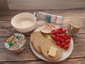 Zdjęcie przedstawia Dietę o kontr.zaw.kwasów tłuszczowych: Ryż na mleku Chleb mieszany pszenno-żytni Masło extra 82% Serek wiejski ziarnisty Kawa zbożowa z mlekiem Woda źródlana 1 szt Sałata zielona  Pomidorki koktajlowe Szynka Piastowska- wp., wędzona, parzona z dod. b.sojowego i wody